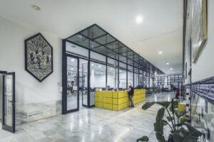Recepción interior de Casa Caridad, con mostrador amarillo, paredes de azulejos blancos y azules y el emblema histórico de la Asociación Valenciana de Caridad.