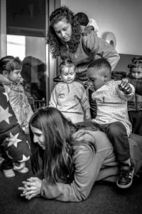 Imagen en blanco y negro en la que mujeres y niños pequeños participan juntos en una actividad de juego en el aula.